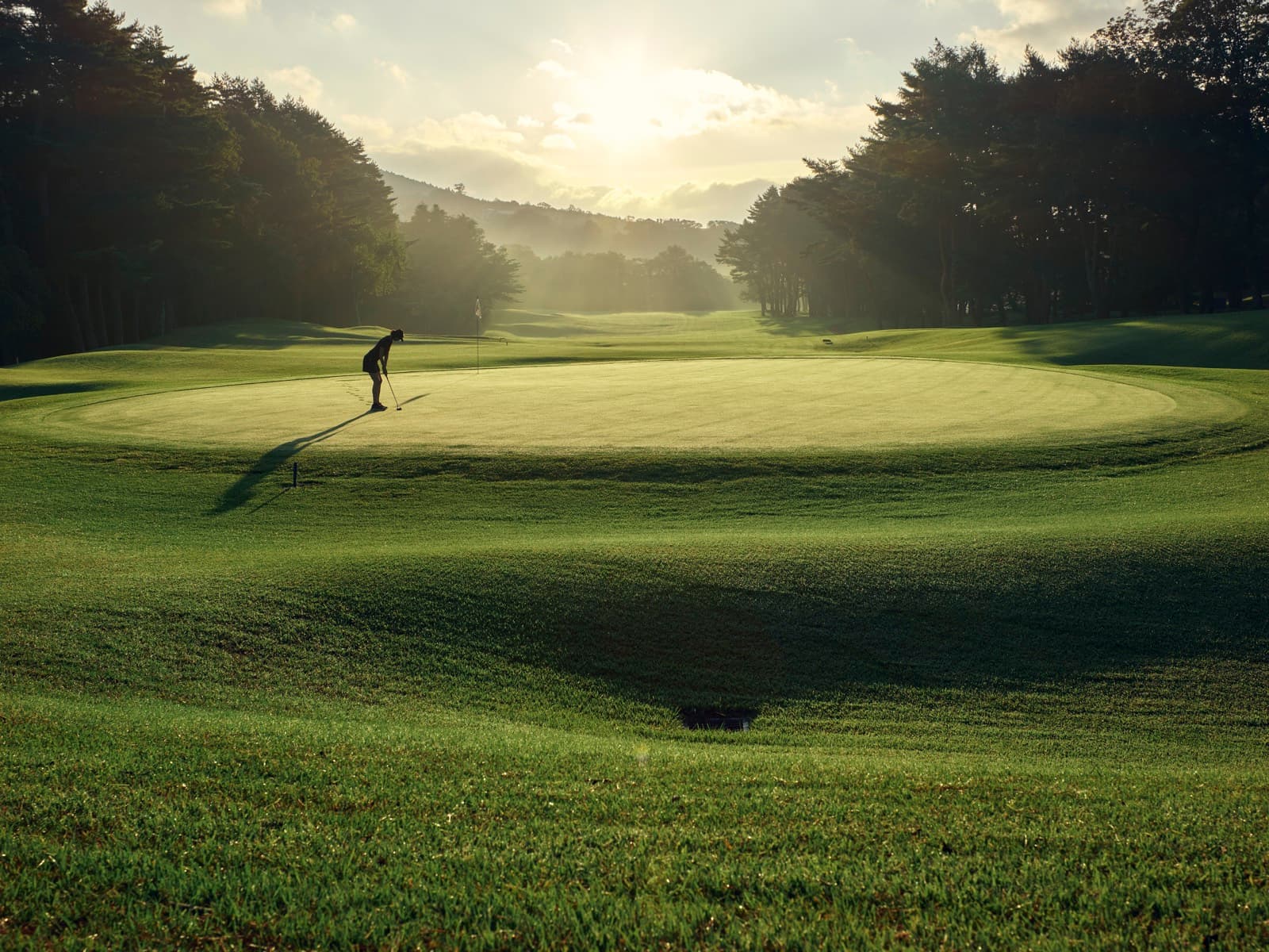 Golfer putting on a Kagosaka Course green at golden hour